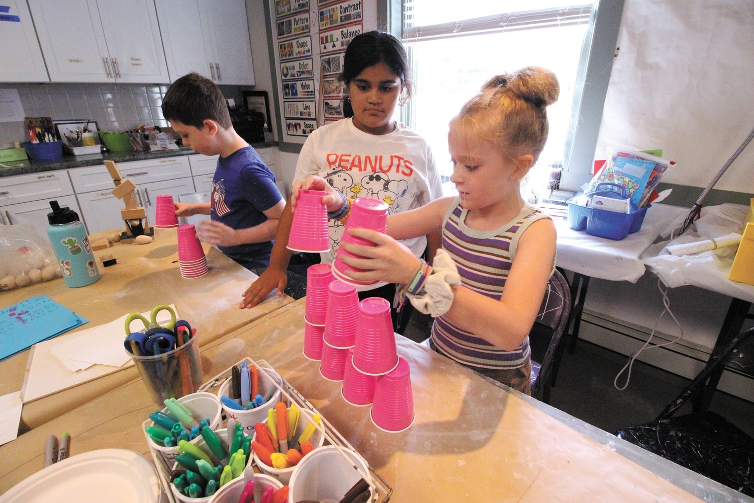A MATTER OF AGILITY: Emmett Revens with Selina Genao looking on and Madelyn Hallett play a game of stacking and then just as quickly collecting plastic cups in a break from exercise their more creative talents.